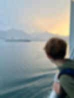 boy on ferry looking across the sea to a ferry and mountains in the distance